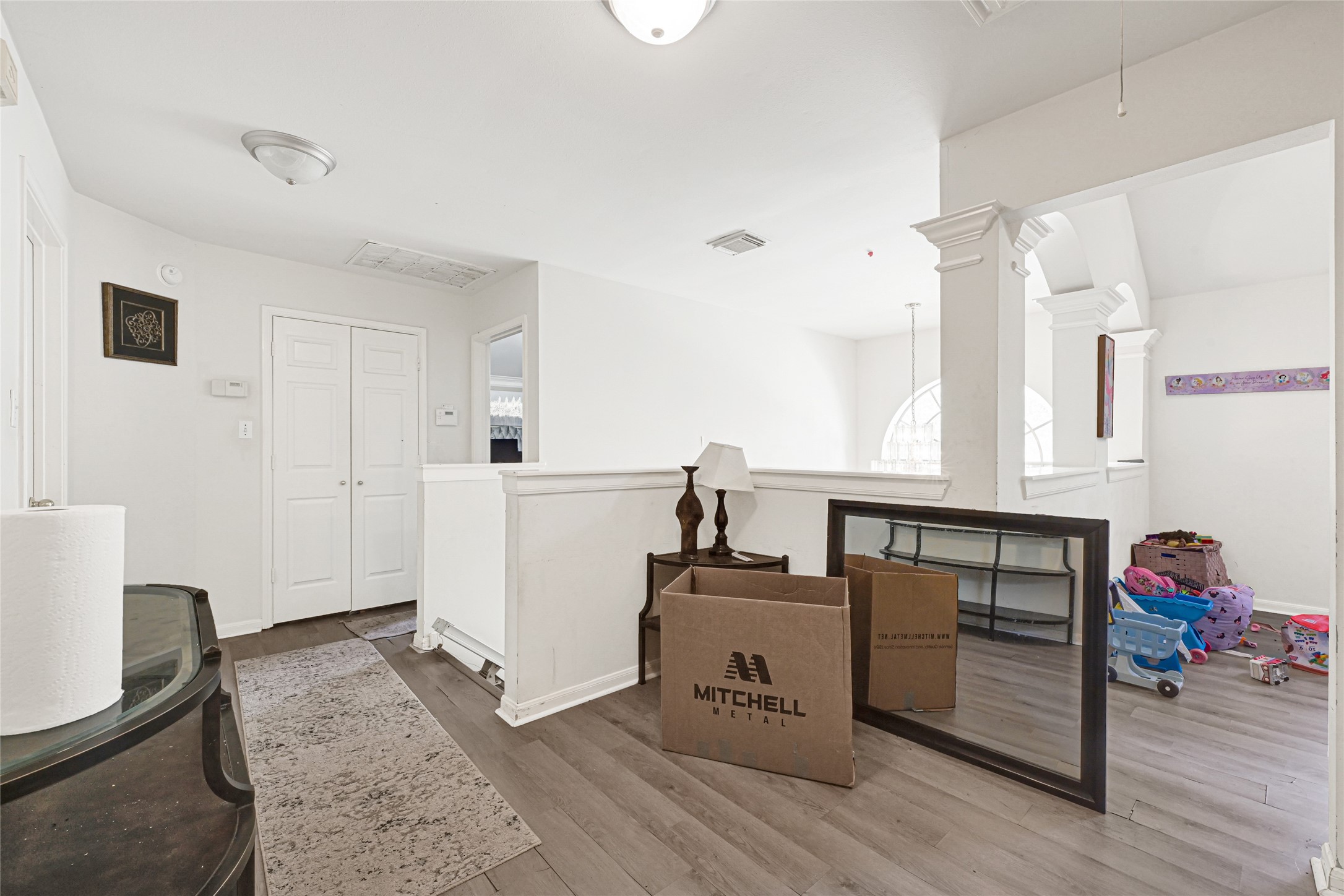 6419 Slate Stone Street Houston, TX 77084 - Photo 19 of 49 This photo showcases a bright, open landing or hallway area with light-colored walls and wood flooring. It features a double-door closet, decorative columns, and ample natural light from a large, arched window. The space has potential for a small play area or additional seating.