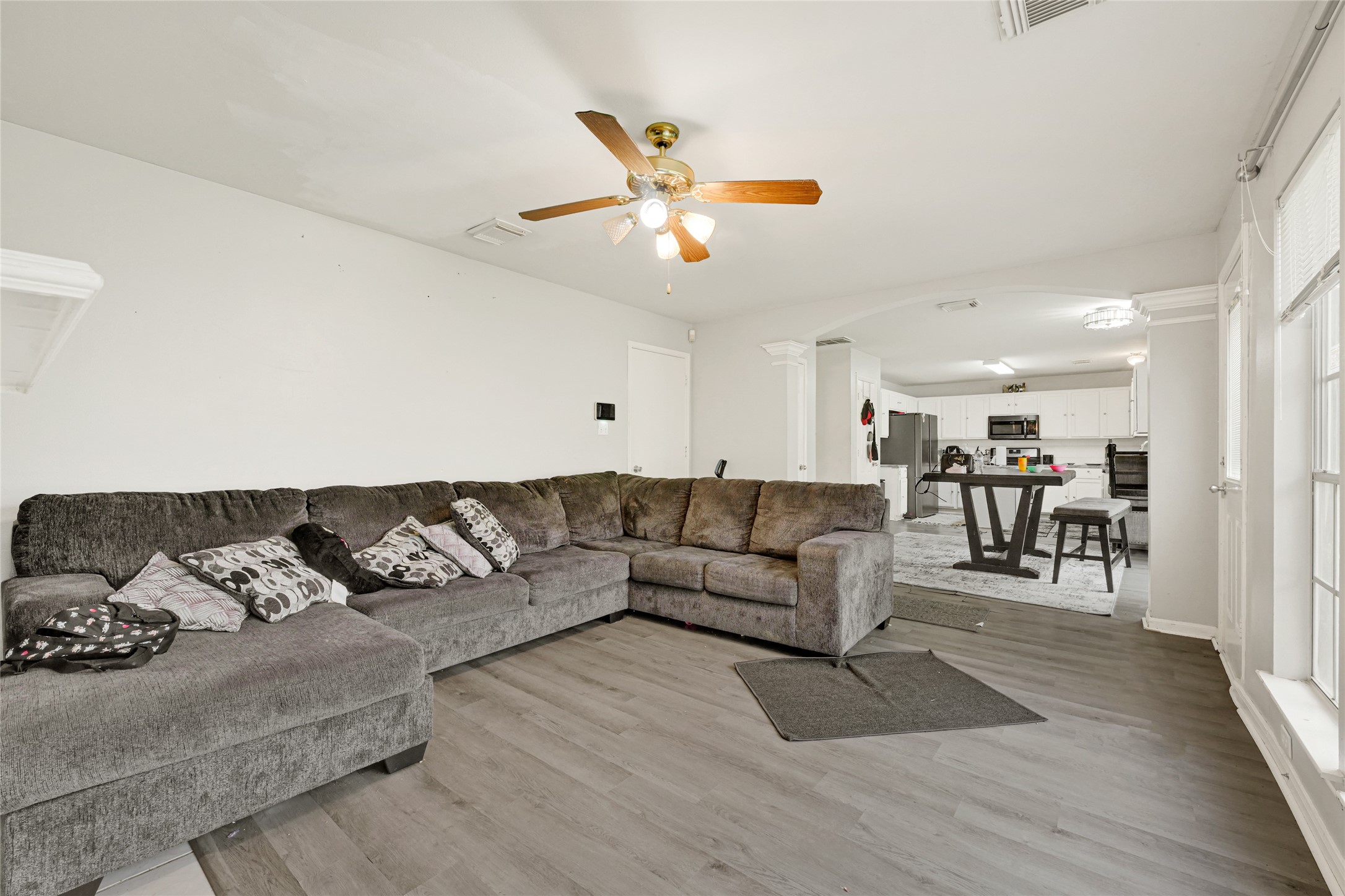 6419 Slate Stone Street Houston, TX 77084 - Photo 49 of 49 This spacious living area features a large sectional sofa, ceiling fan, and abundant natural light from the adjacent windows. The open floor plan seamlessly connects to the dining area and modern kitchen, creating an inviting space for relaxation and entertaining.