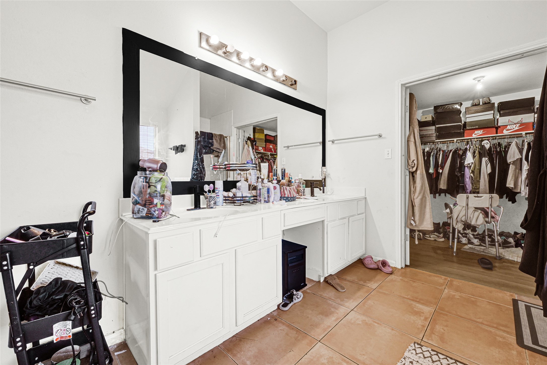6419 Slate Stone Street Houston, TX 77084 - Photo 20 of 49 This photo features a spacious bathroom with a large vanity area, ample counter space, and a sizable mirror. Adjacent is a walk-in closet with abundant shelving and hanging space, ideal for organized storage. The neutral color palette and tile flooring enhance the room's practicality and style.
