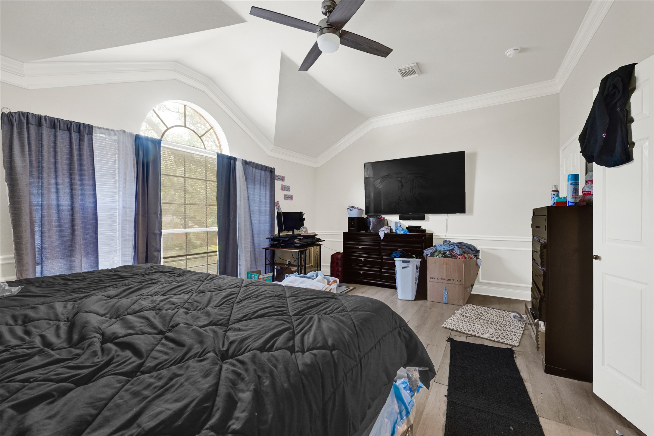 6419 Slate Stone Street Houston, TX 77084 - Photo 21 of 49 This spacious bedroom features high ceilings with a ceiling fan, a large arched window for natural light, and a wall-mounted TV. The room has wood flooring and ample storage with dressers and shelves.
