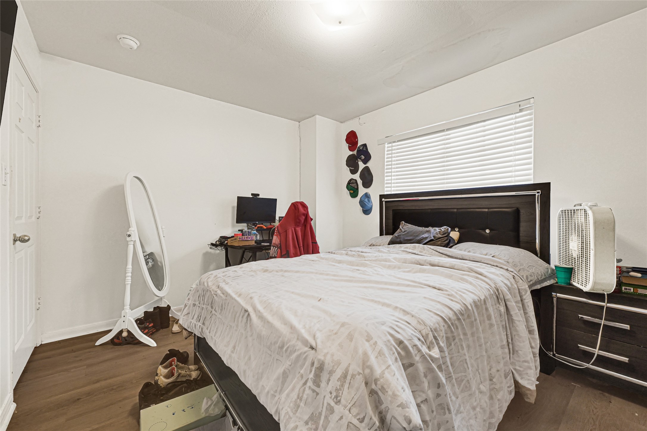 6419 Slate Stone Street Houston, TX 77084 - Photo 24 of 49 This bedroom features a cozy layout with a large bed, ample natural light from a window with blinds, and a neutral color scheme. It includes a wall-mounted hat display, a small office desk setup, and a full-length mirror, offering both functionality and style.