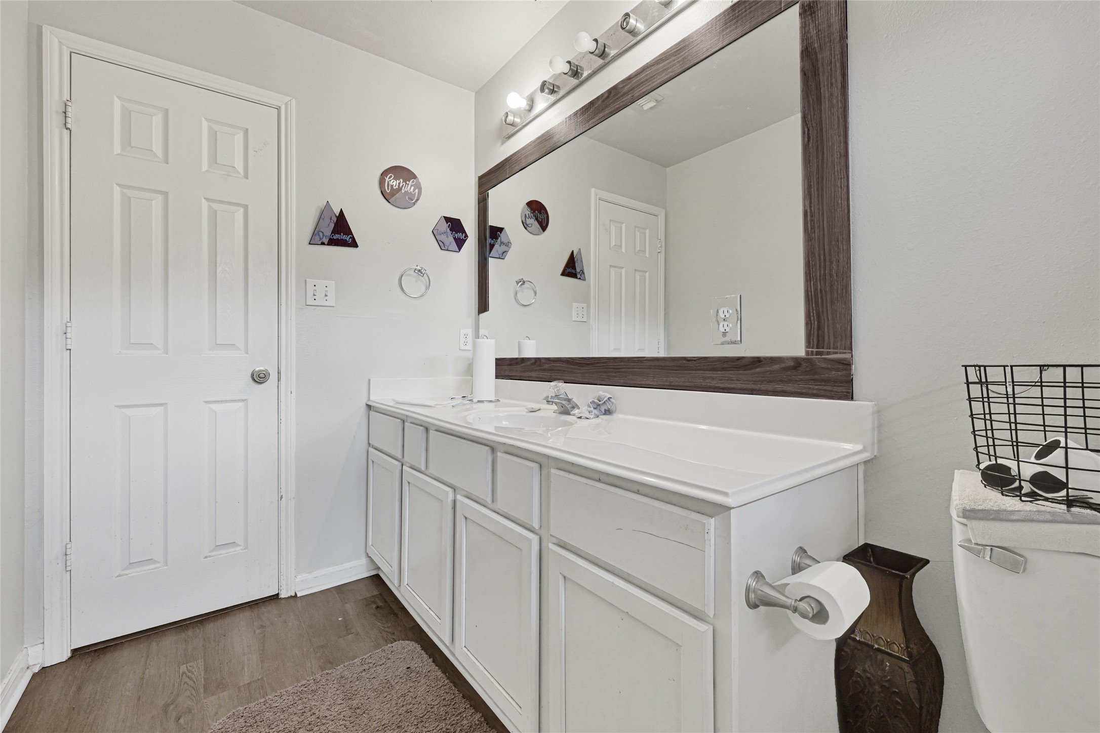 6419 Slate Stone Street Houston, TX 77084 - Photo 26 of 49 This bathroom features a clean, modern design with a large mirror and double vanity. It has white cabinetry, a contemporary light fixture, and a neutral color palette. The hardwood flooring and simple decor add a touch of elegance.