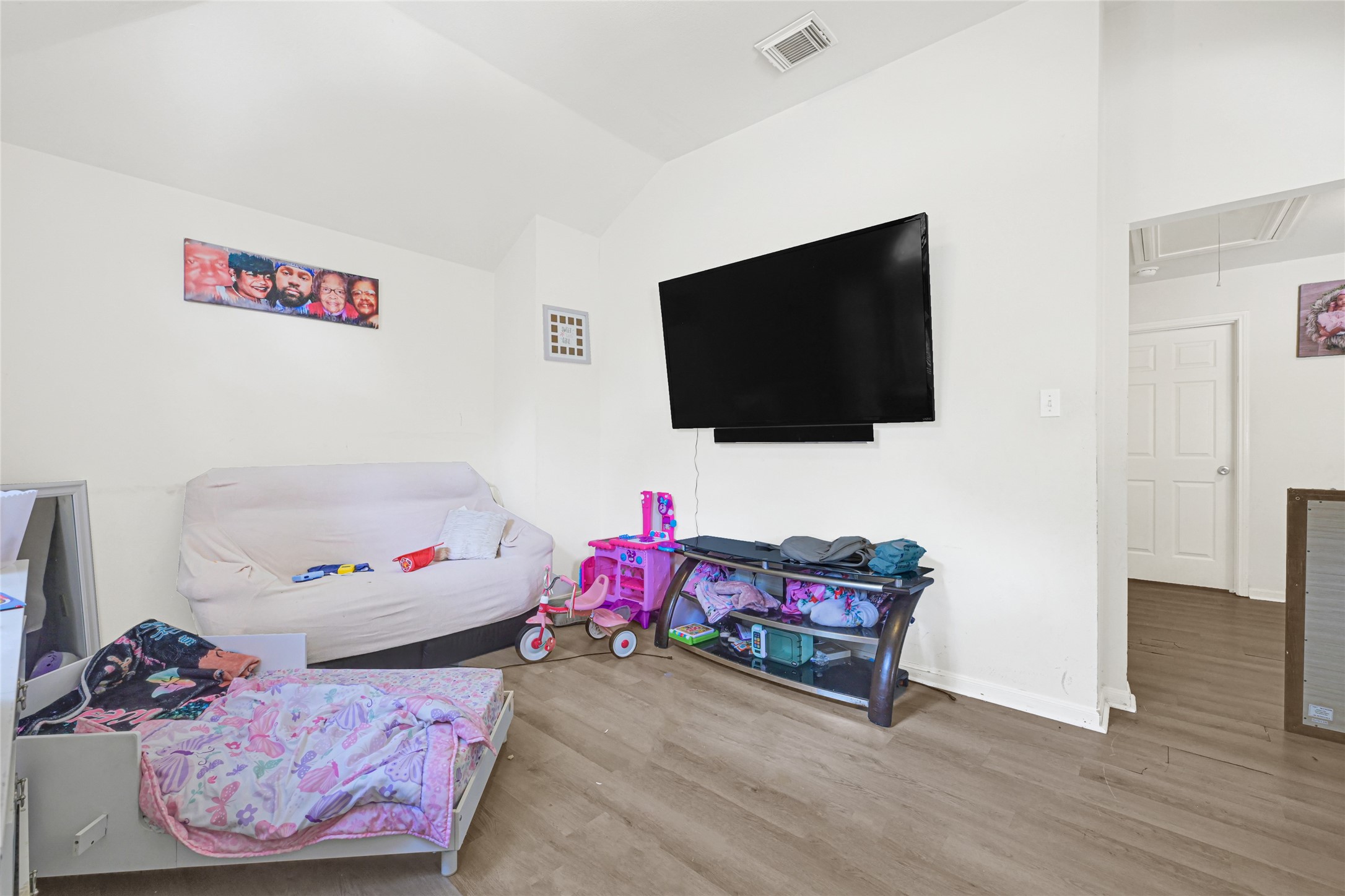 6419 Slate Stone Street Houston, TX 77084 - Photo 30 of 49 A cozy room with light wood flooring, featuring a wall-mounted TV and a sofa. The space includes a children's play area and simple decor, creating a family-friendly atmosphere.