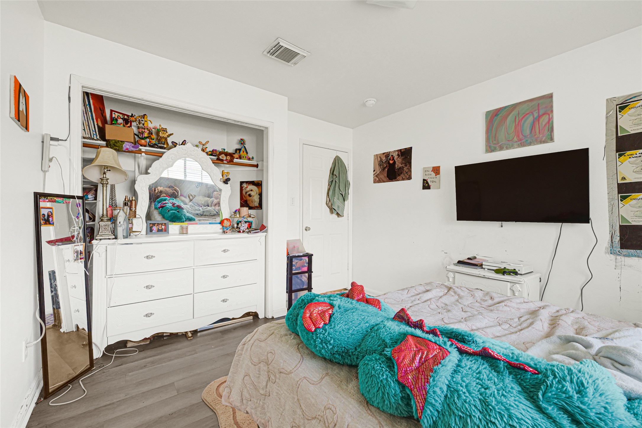 6419 Slate Stone Street Houston, TX 77084 - Photo 35 of 49 This bedroom features a cozy layout with light-colored walls and laminate flooring. It includes a white dresser with a mirror, a mounted TV, and ample natural light. The space is personalized with decorations and artwork, making it ideal for a child's room.