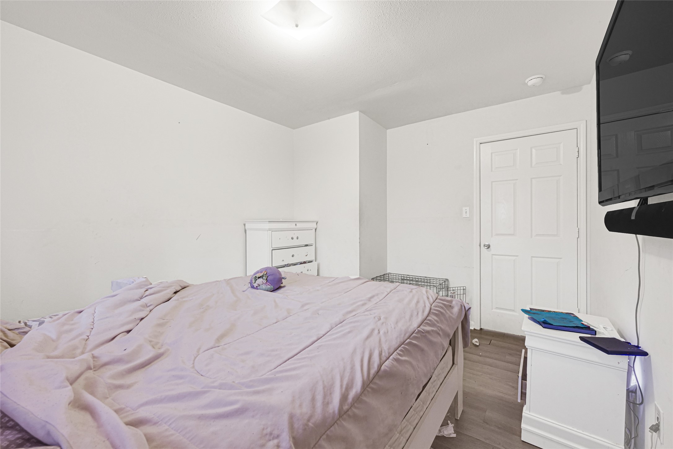 6419 Slate Stone Street Houston, TX 77084 - Photo 37 of 49 This is a cozy bedroom featuring a minimalist design with light-colored walls and flooring. It includes a bed with a pastel comforter, a small dresser, and a wall-mounted TV. There’s also a door leading to another area, enhancing accessibility.