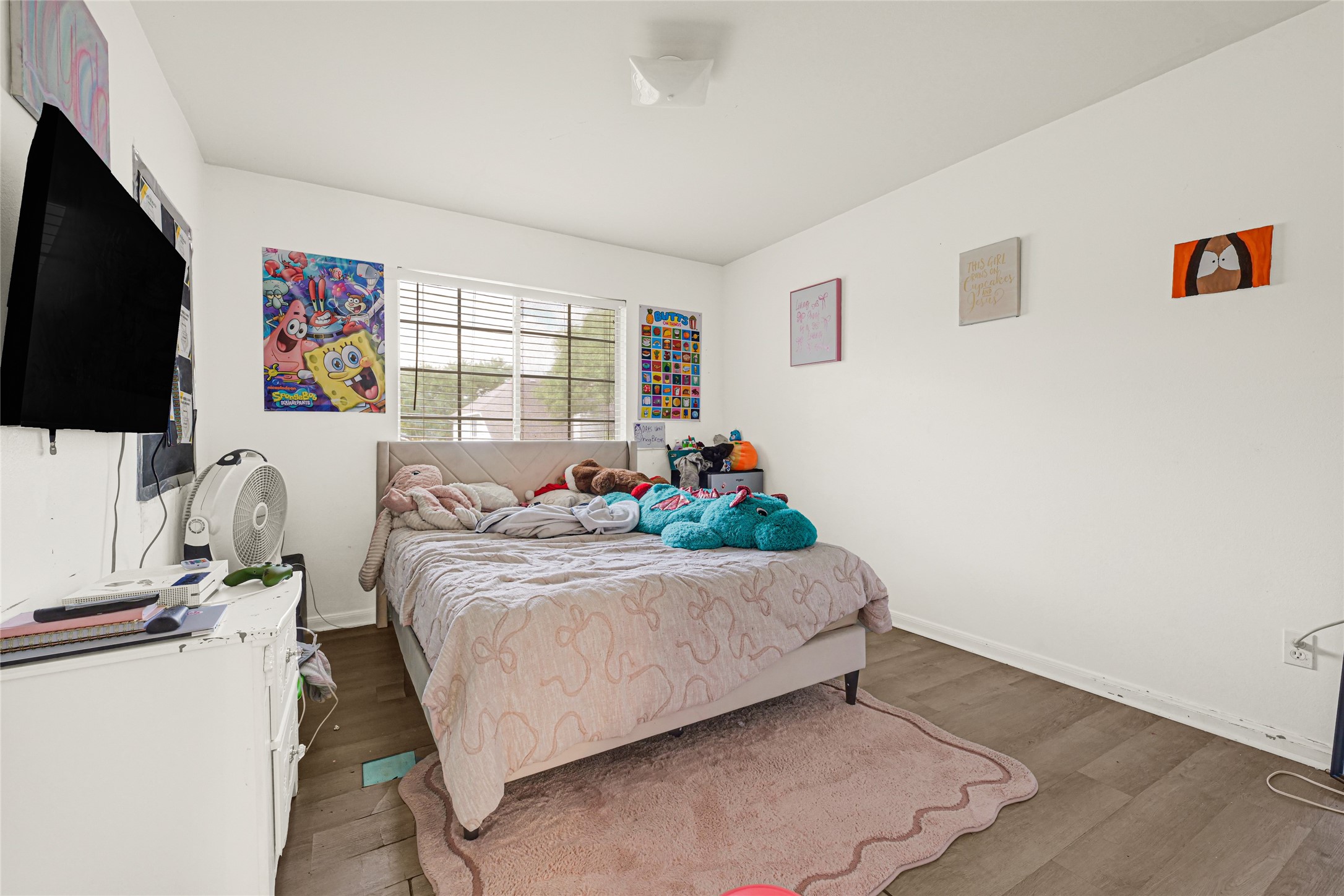 6419 Slate Stone Street Houston, TX 77084 - Photo 38 of 49 This bedroom features bright natural light from a large window, neutral-colored walls, and hardwood flooring. It's cozy and ideal for a child's room, with colorful decor and a mounted TV.