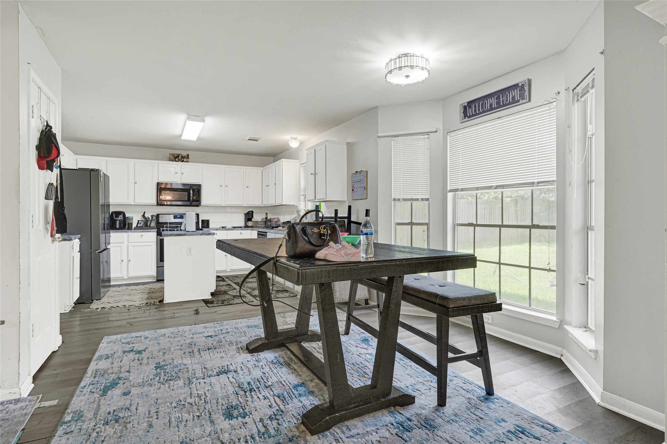 6419 Slate Stone Street Houston, TX 77084 - Photo 3 of 49 This photo shows a bright, open kitchen and dining area with white cabinetry, modern appliances, and large windows providing ample natural light. The space includes a dark wooden dining table and bench, with a welcoming, homey atmosphere.