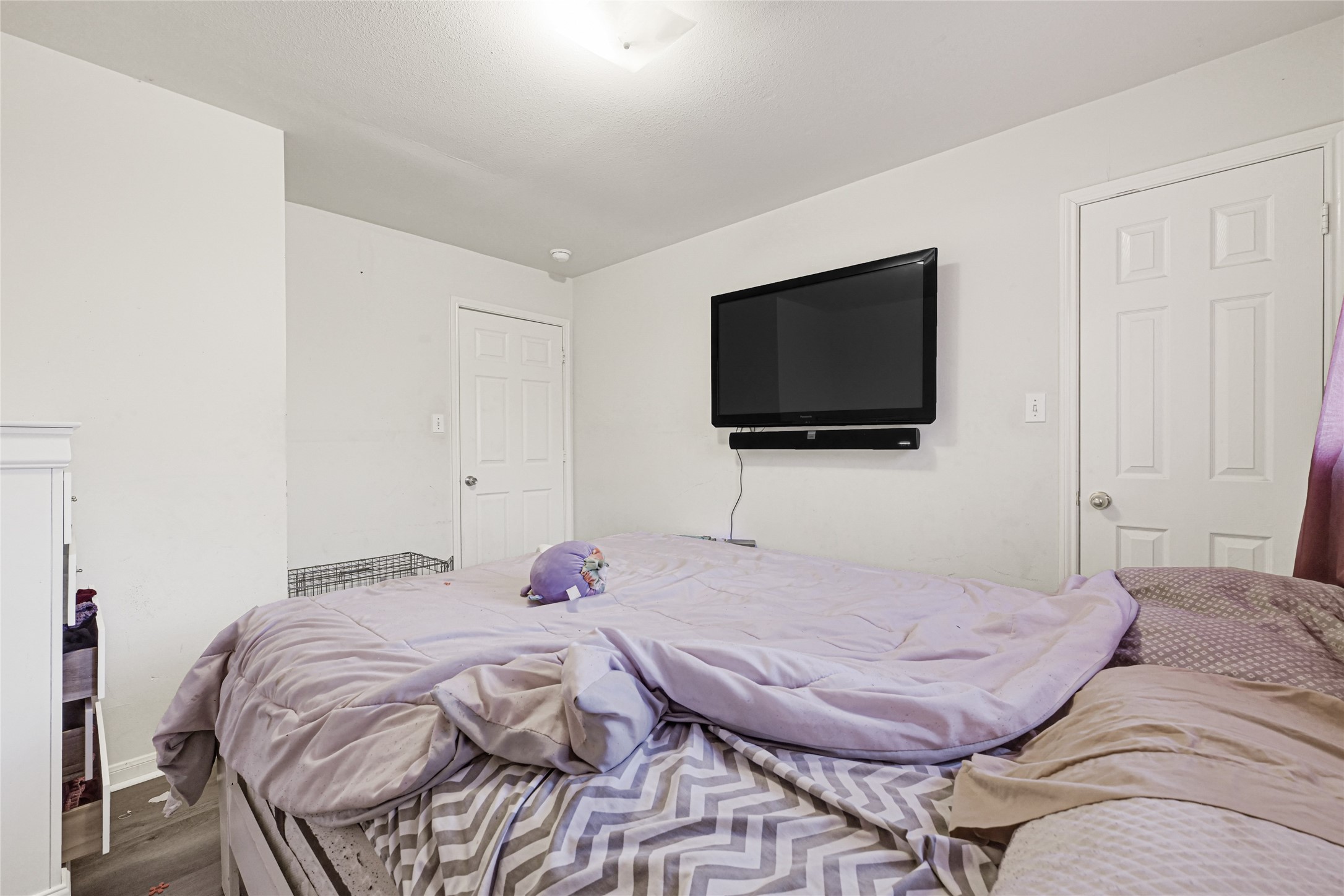 6419 Slate Stone Street Houston, TX 77084 - Photo 40 of 49 Cozy bedroom with neutral walls, featuring a wall-mounted TV and a comfortable bed. Two doors provide access to additional spaces, and natural light filters in through a window with purple curtains. Perfect for relaxation.
