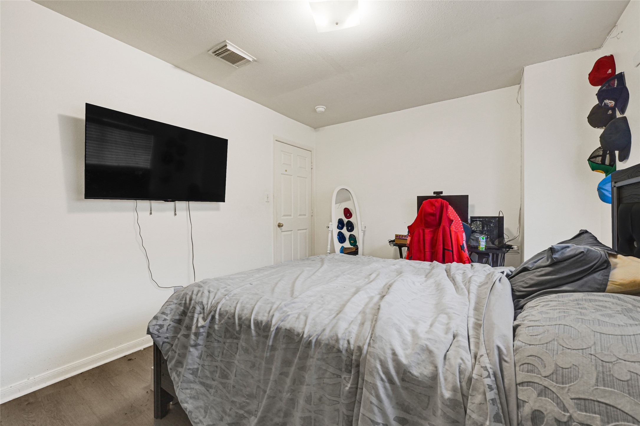 6419 Slate Stone Street Houston, TX 77084 - Photo 41 of 49 This photo shows a cozy bedroom with a mounted TV, a neatly made bed, and a desk area. The room has a simple design with neutral walls, and there's a display of hats on the wall, adding a personal touch.