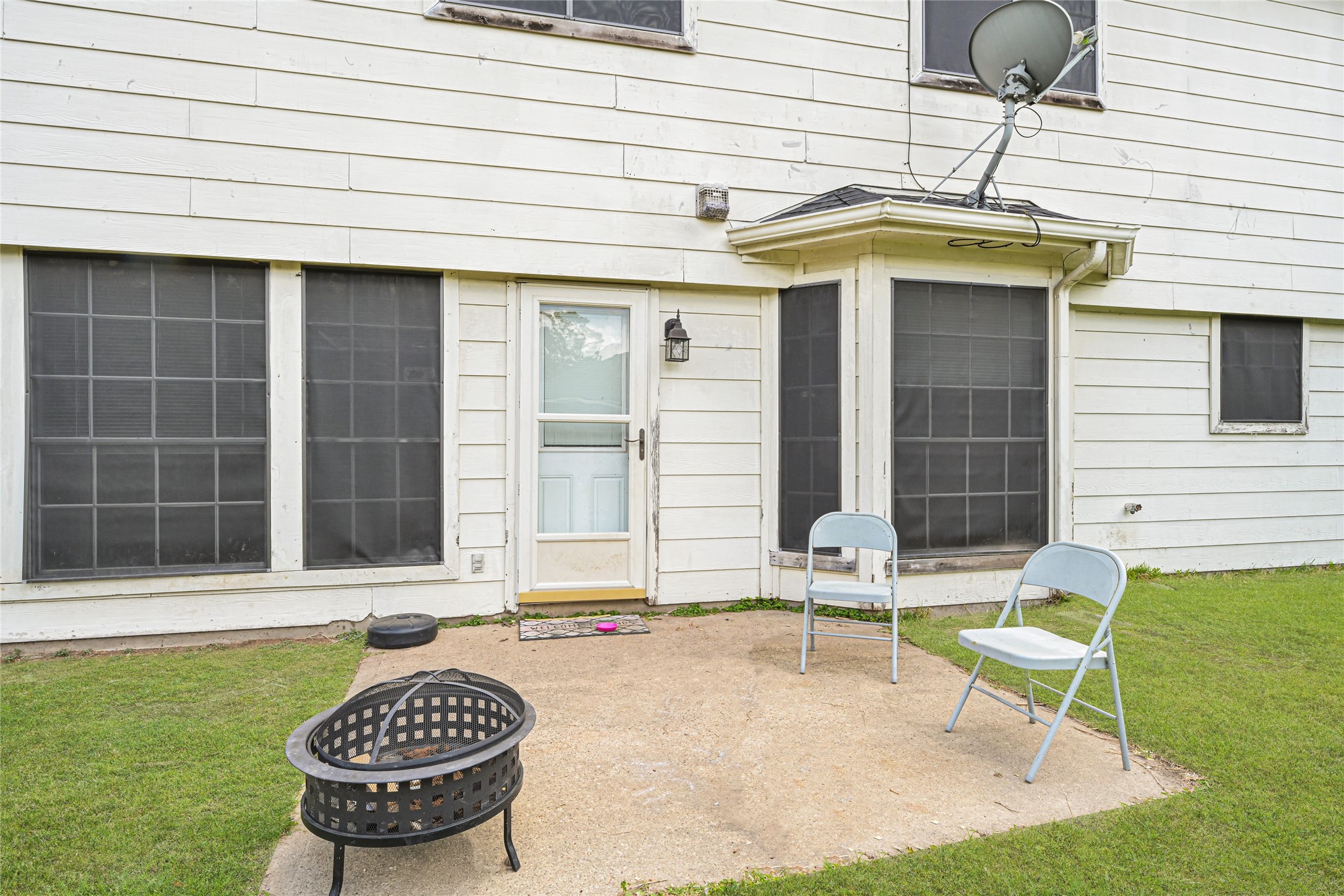6419 Slate Stone Street Houston, TX 77084 - Photo 44 of 49 Outdoor patio area with a concrete slab, two folding chairs, and a fire pit. The exterior features white siding and several large windows, offering a cozy spot for relaxation.