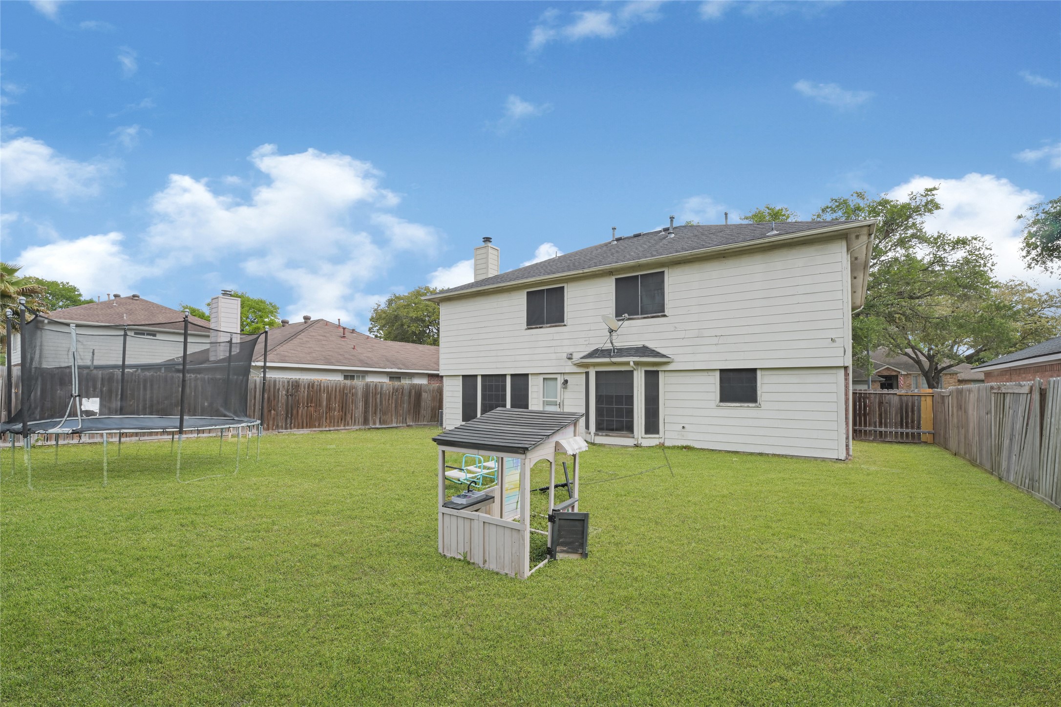 6419 Slate Stone Street Houston, TX 77084 - Photo 45 of 49 Spacious backyard with a well-maintained lawn, enclosed by a wooden fence for privacy. Features a trampoline and a small playhouse, perfect for family activities. The two-story house has a modern exterior with a patio area.