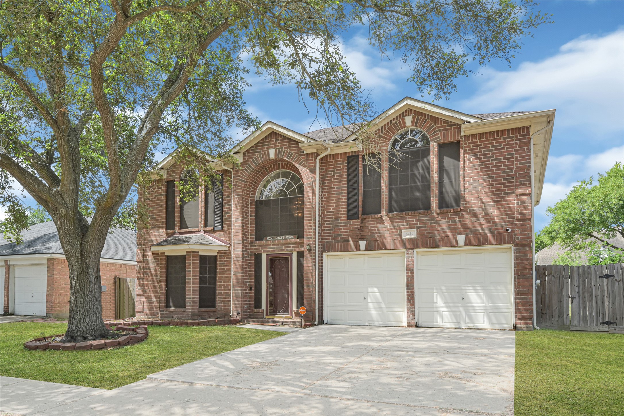 6419 Slate Stone Street Houston, TX 77084 - Photo 47 of 49 This photo shows a two-story brick house with a double garage, large arched windows, and a welcoming front entrance. It features a well-maintained front yard with a mature tree and a spacious driveway.