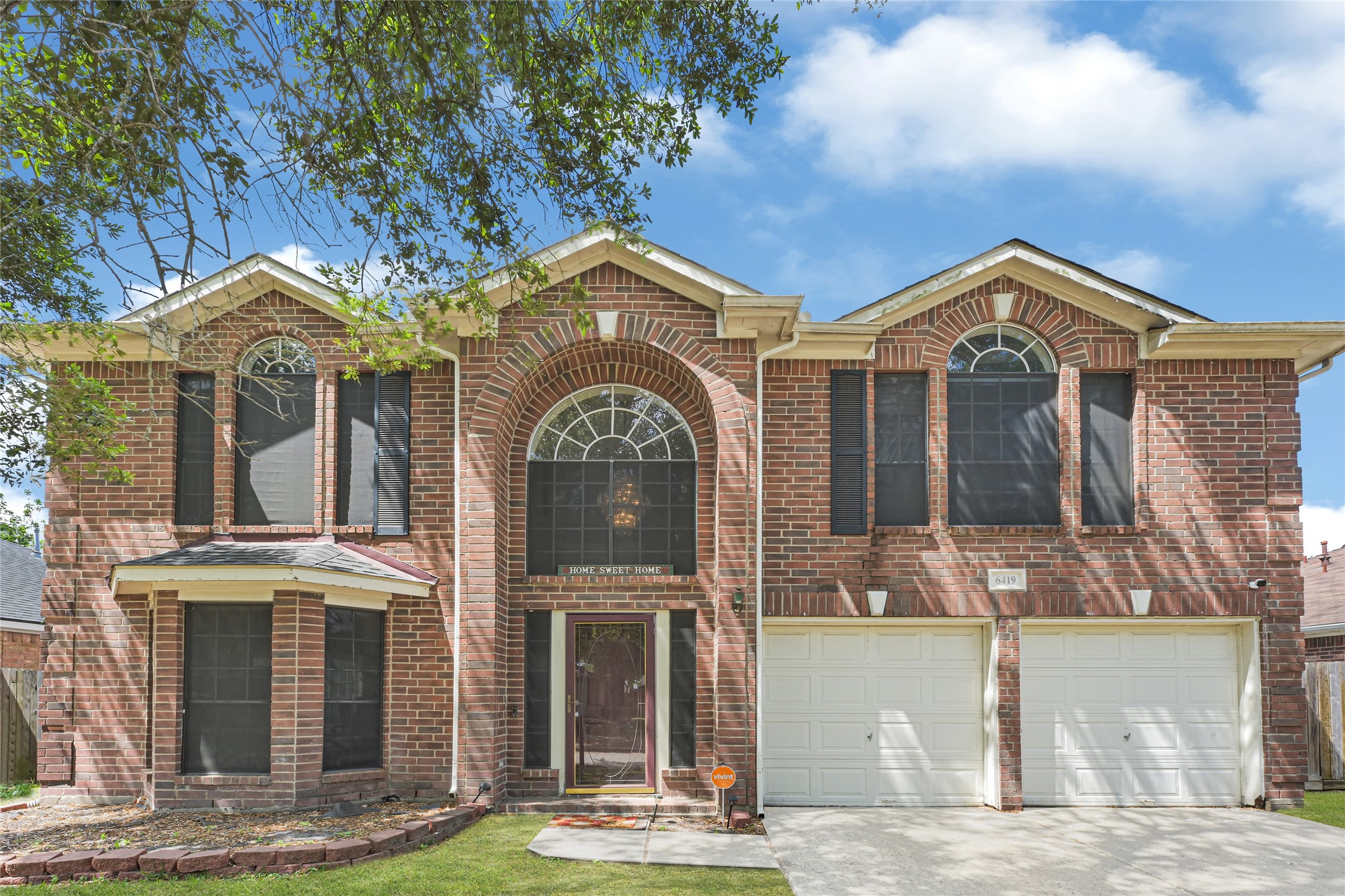 6419 Slate Stone Street Houston, TX 77084 - Photo 48 of 49 This is a two-story brick home featuring a symmetrical facade with large arched windows, a welcoming front porch, and a double garage. The property is surrounded by a well-maintained lawn and mature trees, offering great curb appeal.