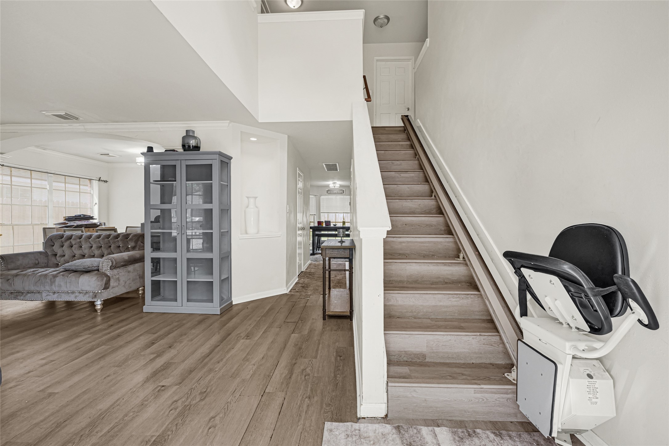 6419 Slate Stone Street Houston, TX 77084 - Photo 4 of 49 This photo showcases a bright, open living area with wood flooring, a cozy couch, and a modern glass cabinet. A wooden staircase with a chairlift leads upstairs, adding convenience and accessibility to the home.