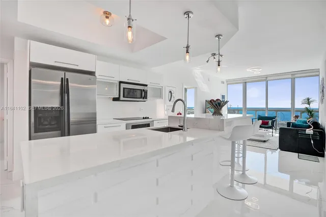 a kitchen with stainless steel appliances kitchen island granite countertop a refrigerator a sink a stove and white cabinets with wooden floor