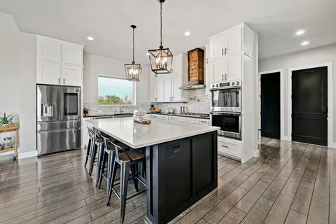 a kitchen with stainless steel appliances kitchen island granite countertop a refrigerator a stove a sink and a wooden floors
