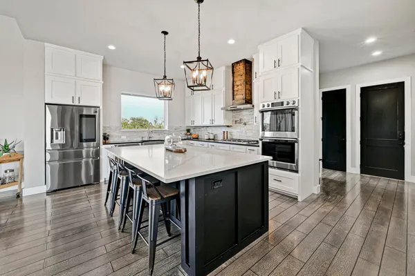 a kitchen with stainless steel appliances kitchen island granite countertop a refrigerator a stove a sink and a wooden floors