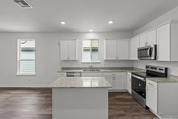 a kitchen with stainless steel appliances granite countertop a stove top oven a sink dishwasher and white cabinets with wooden floor