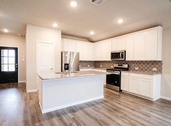 a kitchen with stainless steel appliances granite countertop a stove top oven a sink a refrigerator white cabinets and wooden floor
