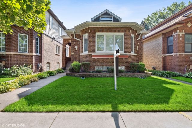 a view of a brick house with a yard plants and a large tree