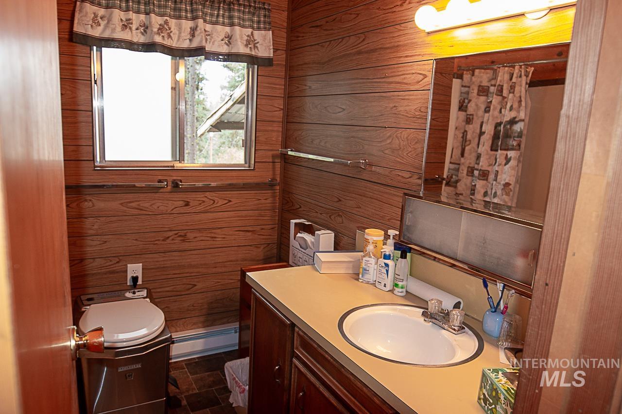 225 Mesplie Road Placerville, ID 83666 - Photo 8 of 39 Full bath featuring vanity, wooden walls, a baseboard radiator, and dark stone finish flooring