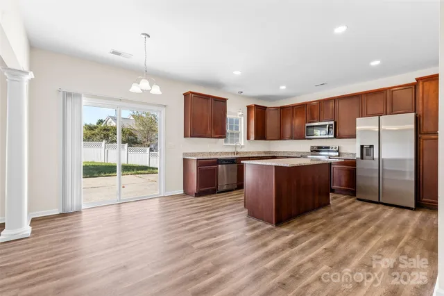 a kitchen with stainless steel appliances granite countertop a refrigerator a sink dishwasher a stove and a large countertops with wooden floor