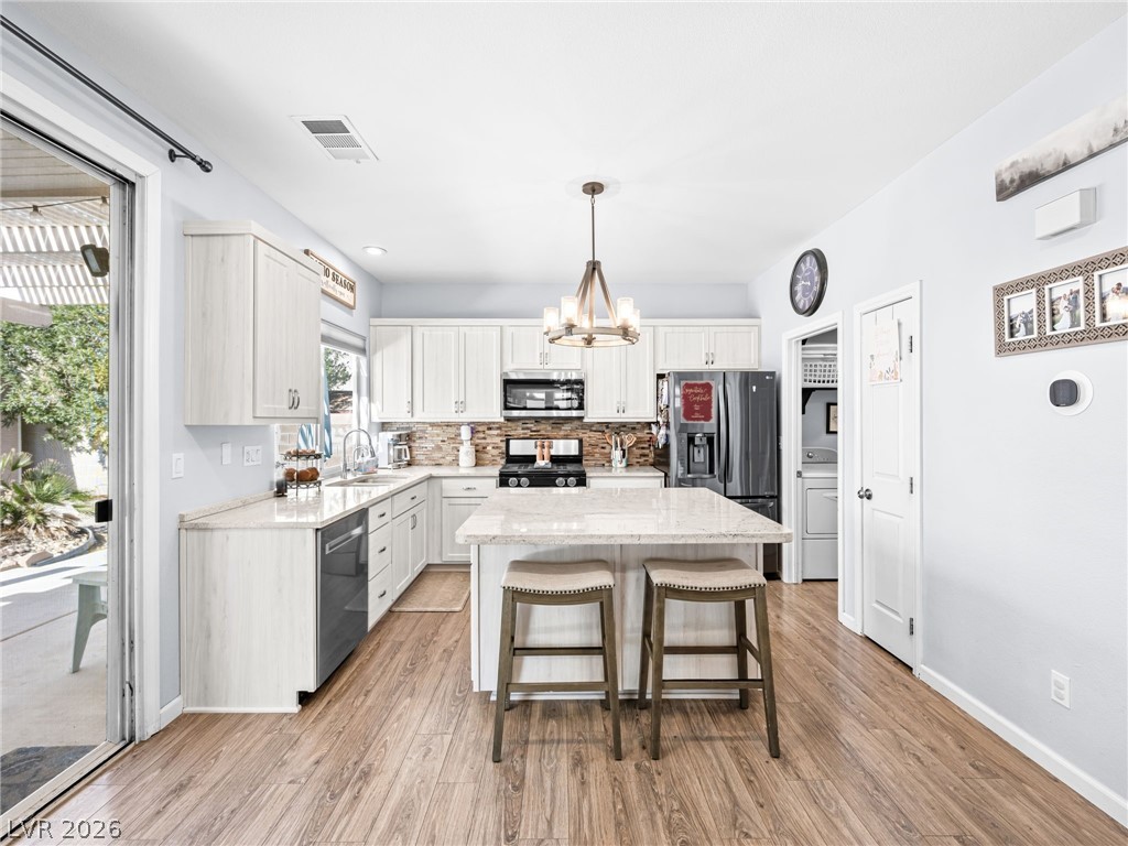 2199 Maple Shade Street Henderson, NV 89002 - Photo 15 of 75 Updated kitchen showcasing refaced cabinets, a stylish backsplash, center island, stainless steel appliances, and durable luxury vinyl plank flooring.