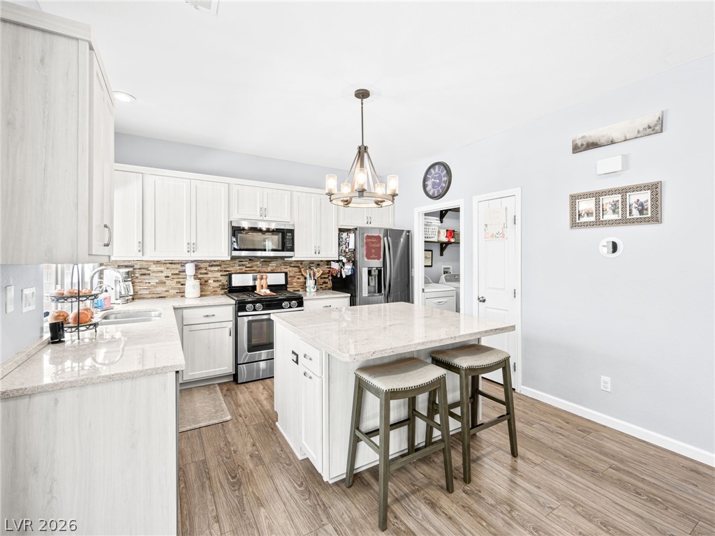 2199 Maple Shade Street Henderson, NV 89002 - Photo 16 of 75 Updated kitchen showcasing refaced cabinets, a stylish backsplash, center island, stainless steel appliances, and durable luxury vinyl plank flooring.