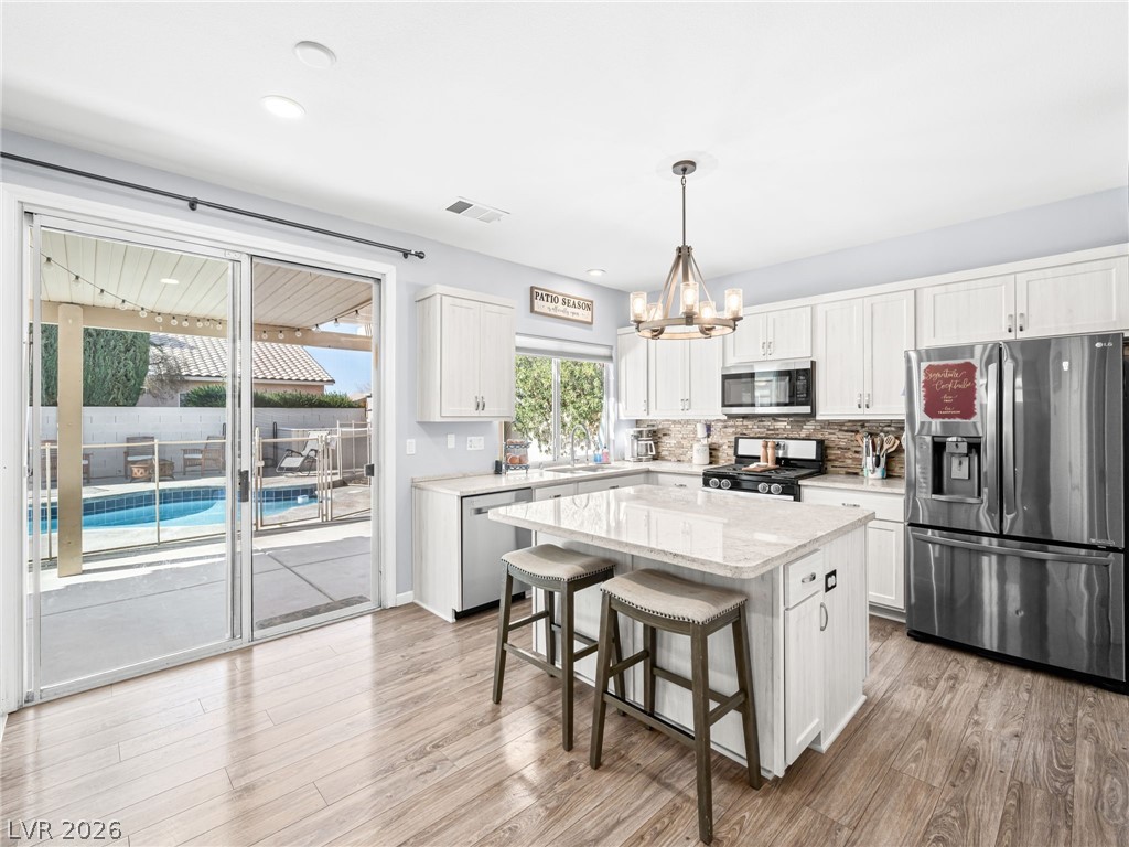 2199 Maple Shade Street Henderson, NV 89002 - Photo 17 of 75 Updated kitchen showcasing refaced cabinets, a stylish backsplash, center island, stainless steel appliances, and durable luxury vinyl plank flooring.