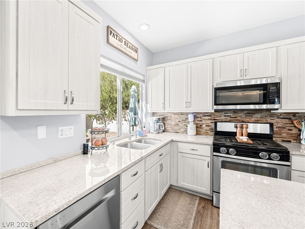 2199 Maple Shade Street Henderson, NV 89002 - Photo 18 of 75 Updated kitchen showcasing refaced cabinets, a stylish backsplash, center island, stainless steel appliances, and durable luxury vinyl plank flooring.