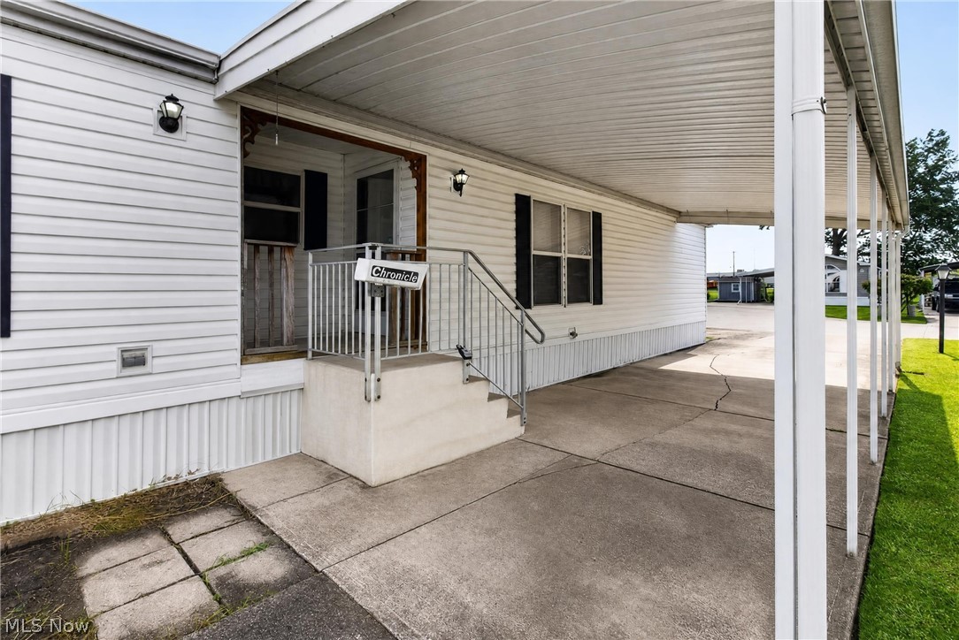 35157 Center Ridge Road, Unit 153 North Ridgeville, OH 44039 - Photo 3 of 35 White siding exterior with black shutters, covered concrete carport, concrete front entry steps with metal handrails, and a covered front porch with exterior lighting