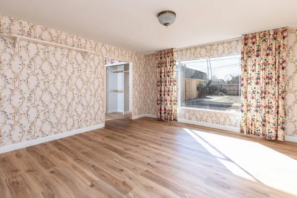 a view of an empty room with a window and wooden floor