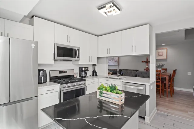 a kitchen with stainless steel appliances kitchen island granite countertop a stove a sink a microwave a refrigerator a dining table and chairs with wooden floor