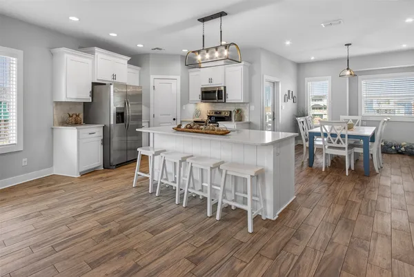 a kitchen with stainless steel appliances granite countertop a dining table chairs refrigerator and microwave