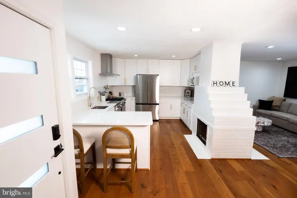 a living room with stainless steel appliances furniture wooden floor and a kitchen view