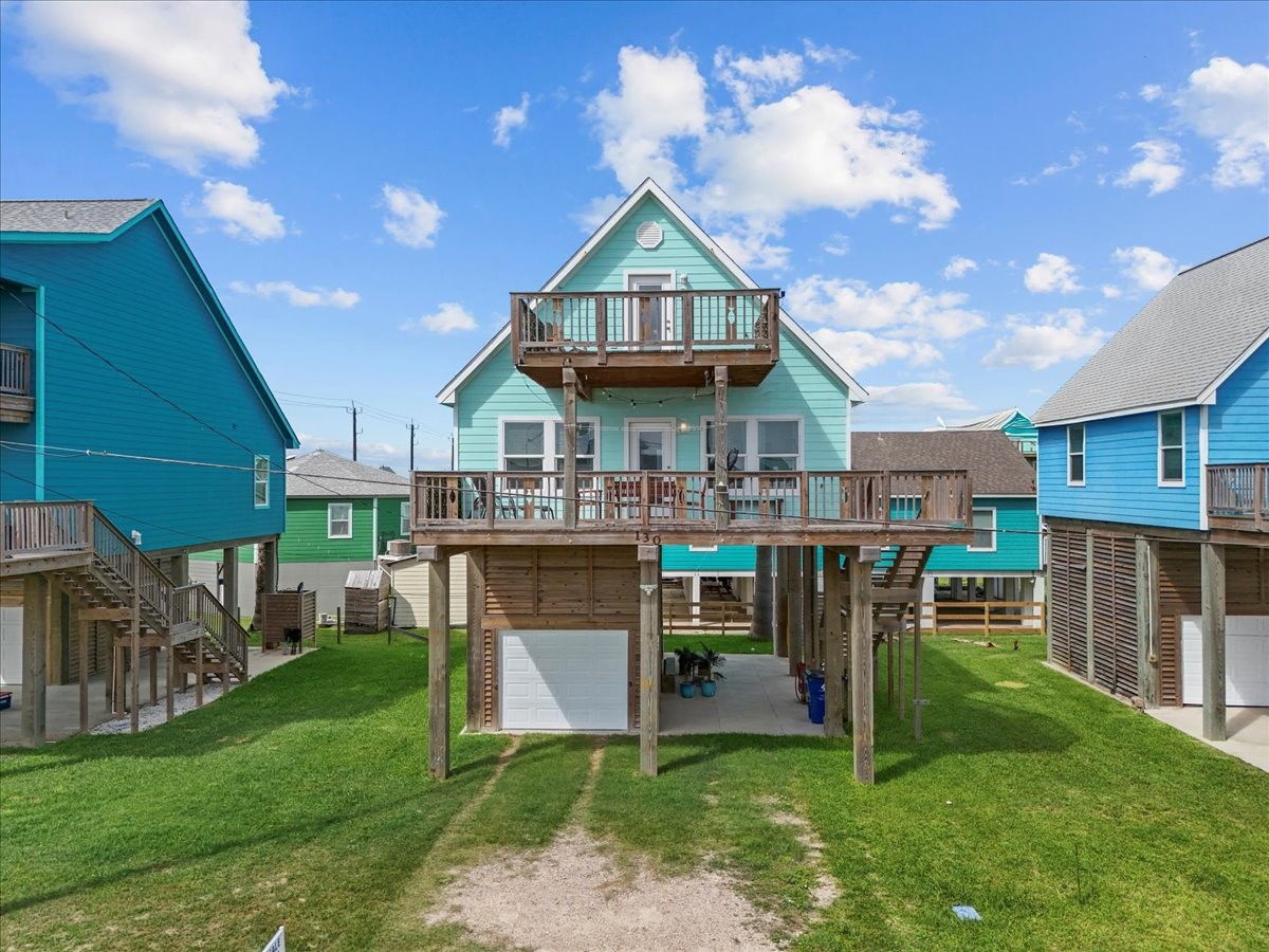 130 Beachcomber Avenue Surfside Beach, TX 77541 - Photo 3 of 33 Elevated coastal home with vibrant exterior, featuring a spacious deck and balcony. The property includes a carport and storage underneath, set in a neighborhood of similar stilt homes. Ideal for beachside living.