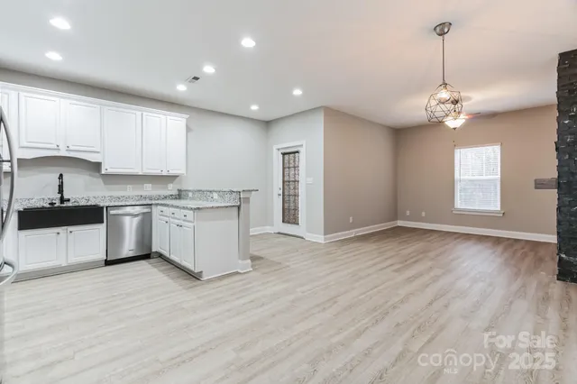 a large kitchen with stainless steel appliances granite countertop a stove a sink dishwasher a refrigerator and white cabinets with wooden floor