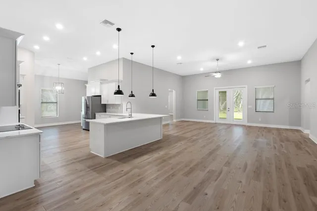 a large room with kitchen island a sink wooden floor white stainless steel appliances and cabinets
