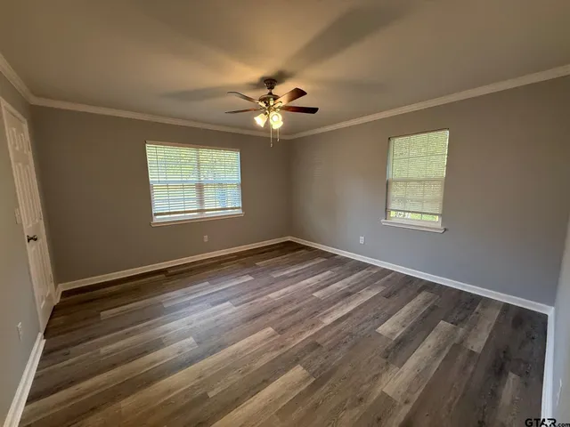 an empty room with wooden floor fan and windows