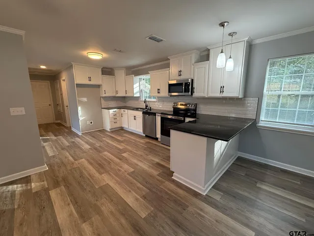 a kitchen with granite countertop a stove a sink a refrigerator and white cabinets with wooden floor