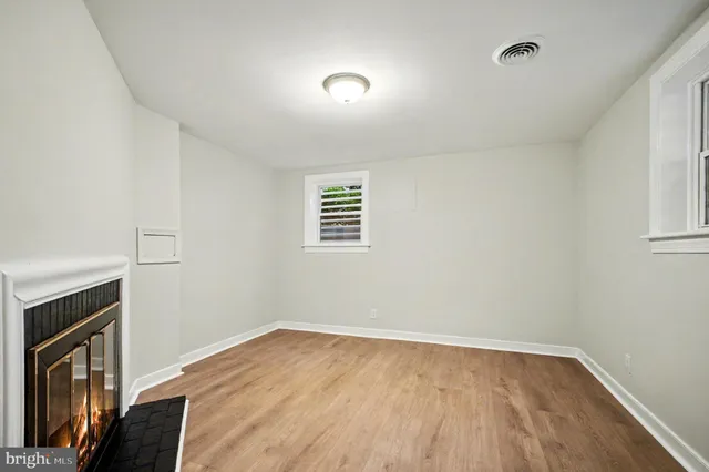 a view of an empty room with wooden floor fireplace and a window