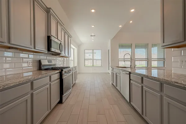 a kitchen with stainless steel appliances granite countertop a sink a stove top oven and wooden floors