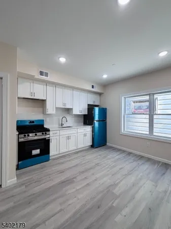 a kitchen with stainless steel appliances granite countertop a stove top oven a refrigerator white cabinets and wooden floor