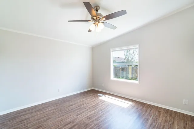 an empty room with wooden floor fan and windows