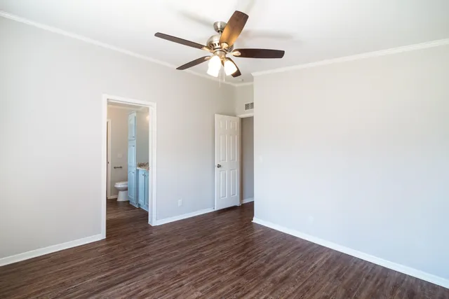 a view of an empty room with wooden floor and a ceiling fan