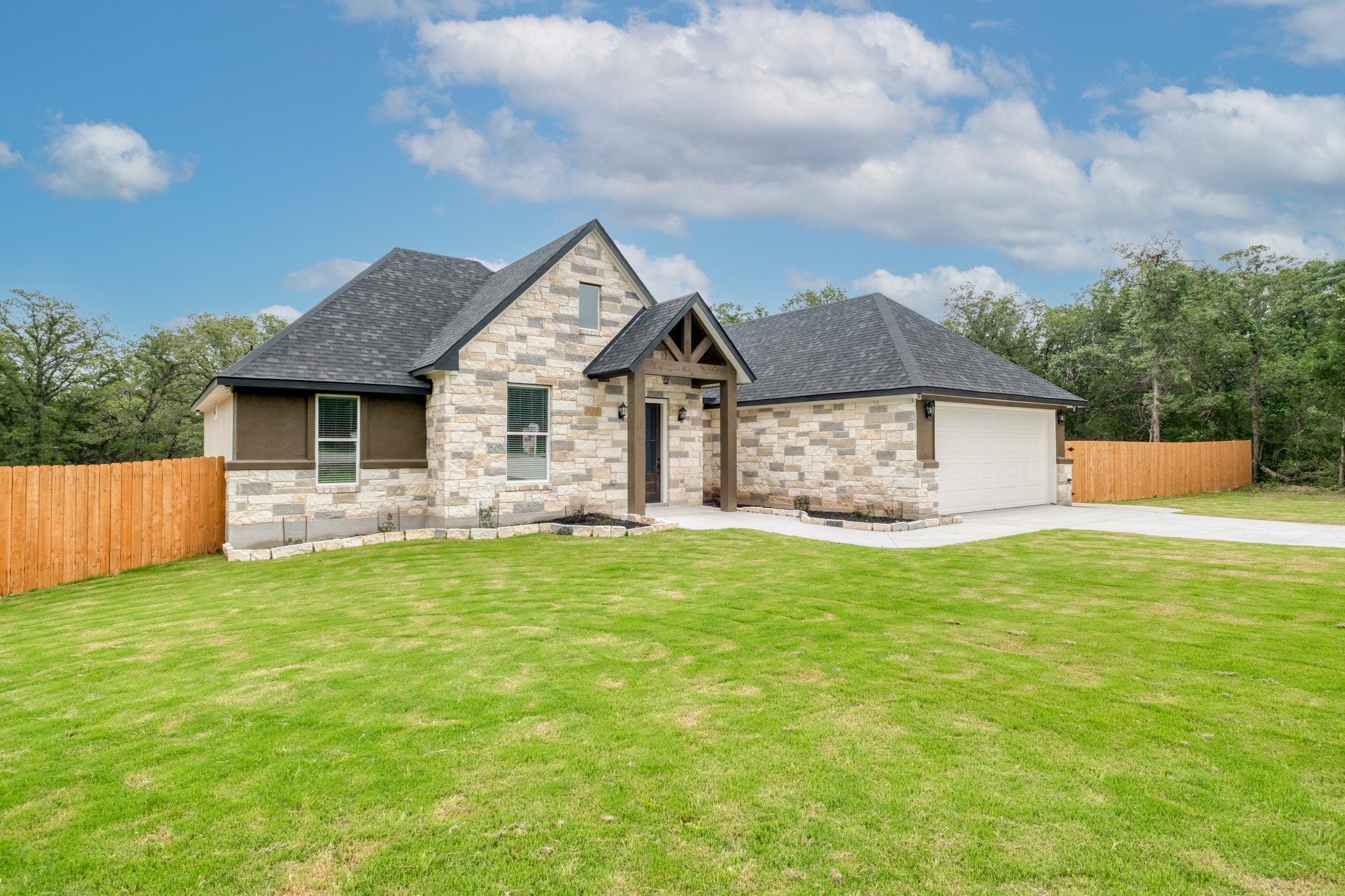 116 Pine Point Cove Elgin, TX 78621 - Photo 2 of 27 Stone and stucco exterior featuring a dark shingle roof, attached garage, covered entryway with timber accents, and a manicured lawn