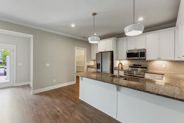 a kitchen with stainless steel appliances granite countertop a refrigerator a sink dishwasher a stove and white cabinets with wooden floor