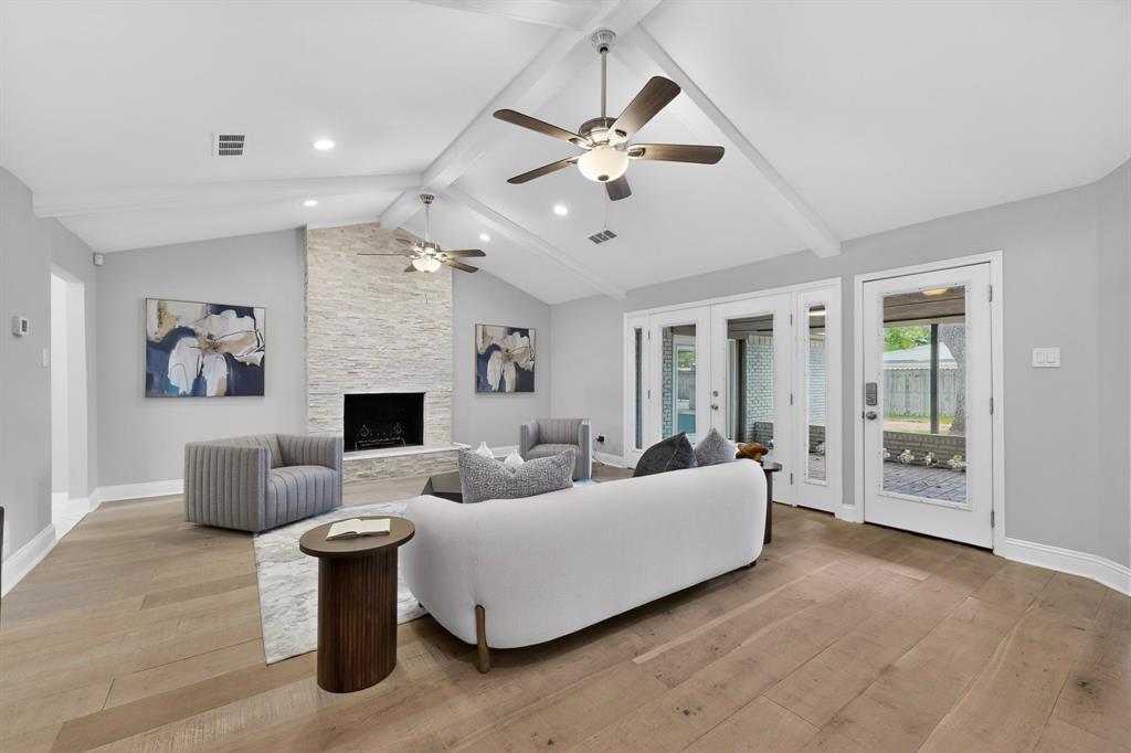 7631 Meadow Road Dallas, TX 75230 - Photo 2 of 40 A cozy family room with a high ceiling, two ceiling fans and a fireplace, with access to the patio at the back.