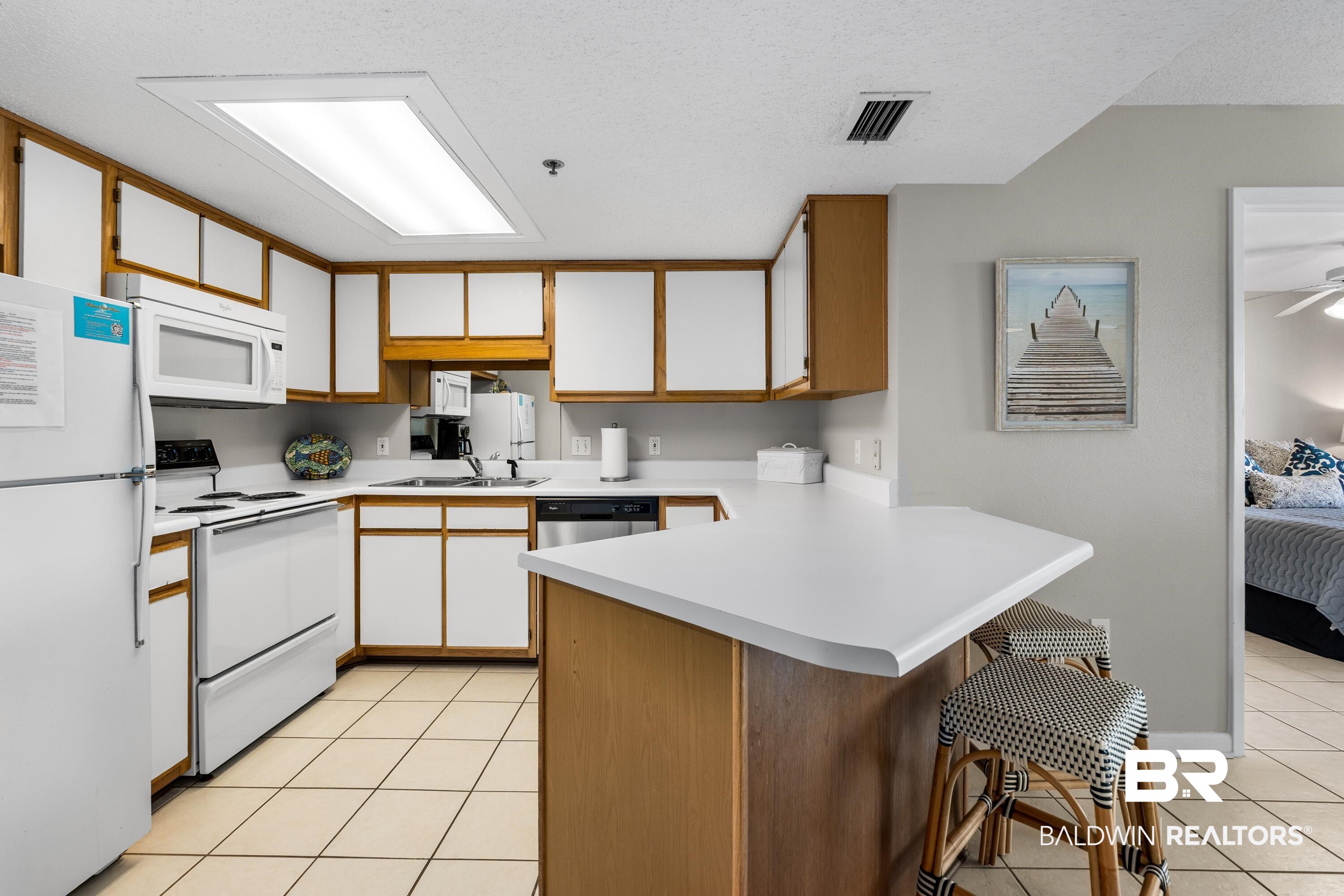 26802 Perdido Beach Boulevard, Unit 406 Orange Beach, AL 36561 - Photo 9 of 37 Kitchen featuring a peninsula, two tone cabinets, light countertops, white appliances, and a kitchen breakfast bar
