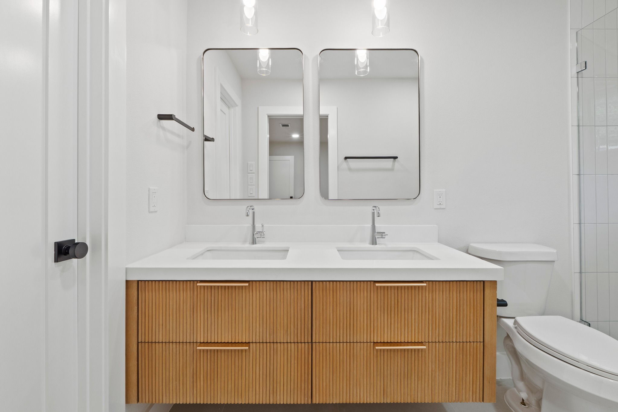 1608 Springer Lane Austin, TX 78758 - Photo 30 of 35 Dual rectangular mirrors above a floating wood-finish vanity with fluted details, white countertop, and integrated sinks